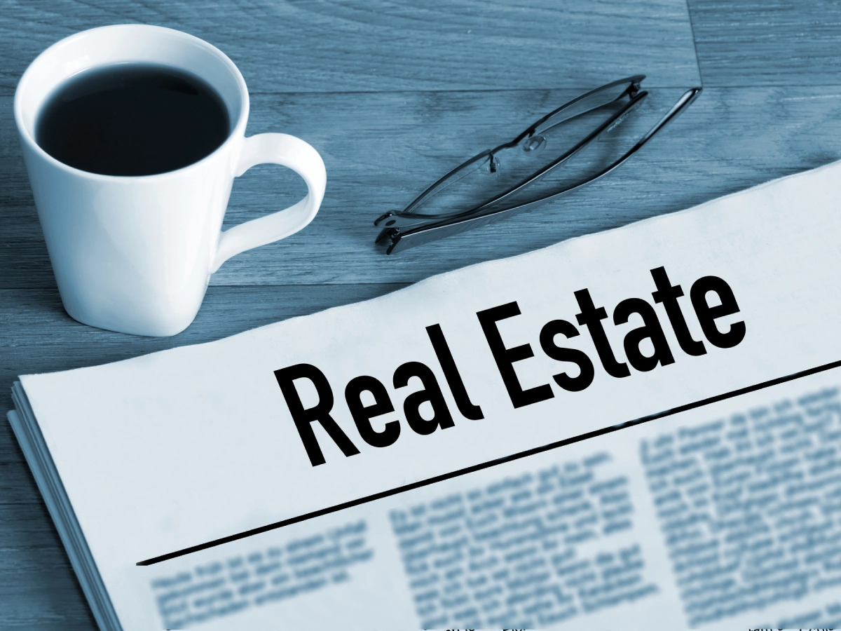 Coffee cup beside real estate news article.
